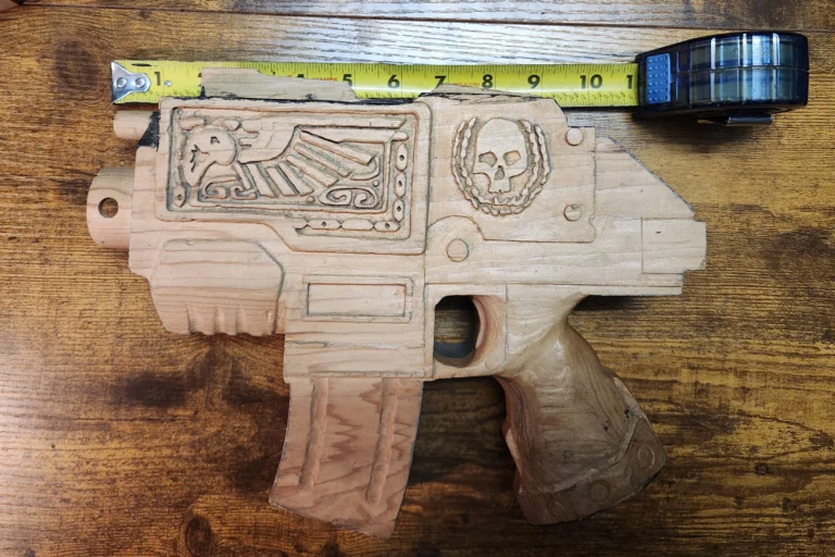 Hand carved Warhammer 40k bolter pistol with measuring tape showing 11inches